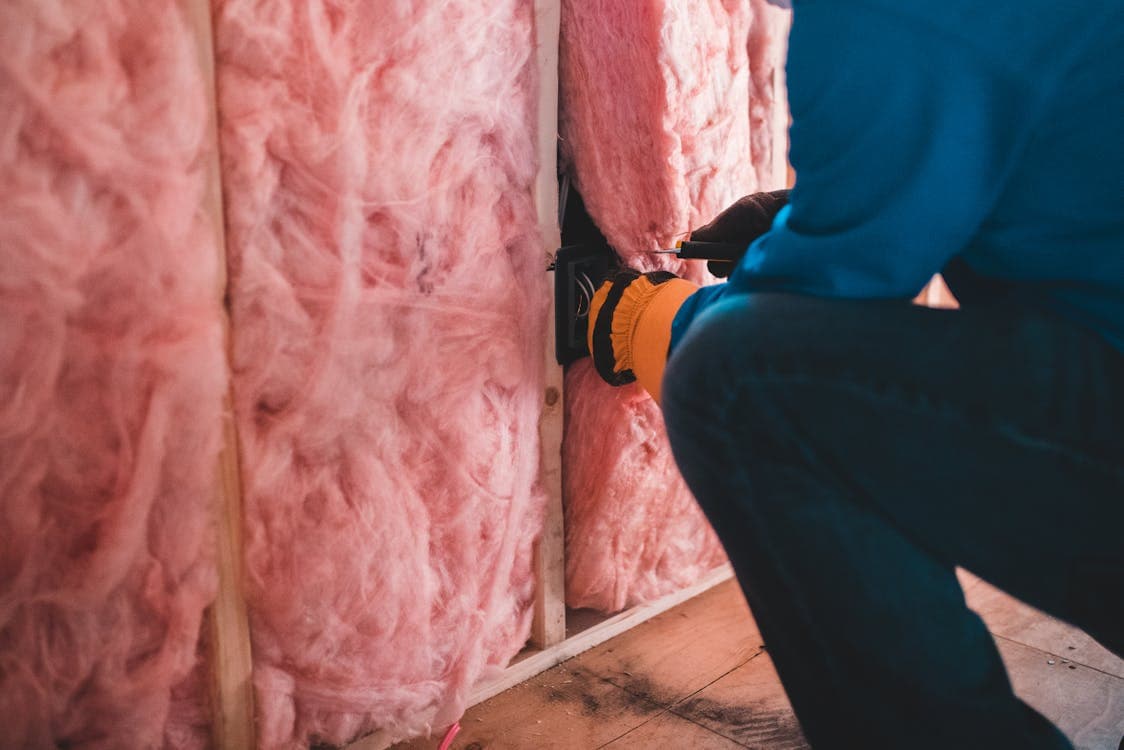 Worker installing pink fiberglass insulation between wall studs