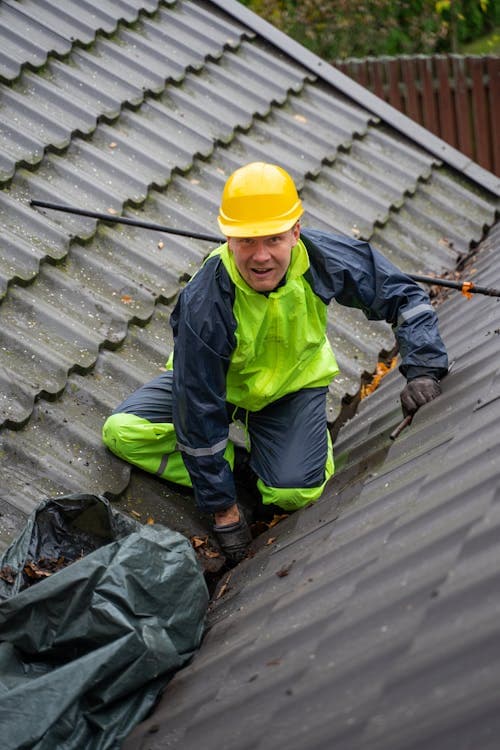 Worker in safety gear cleaning debris from a roof gutter